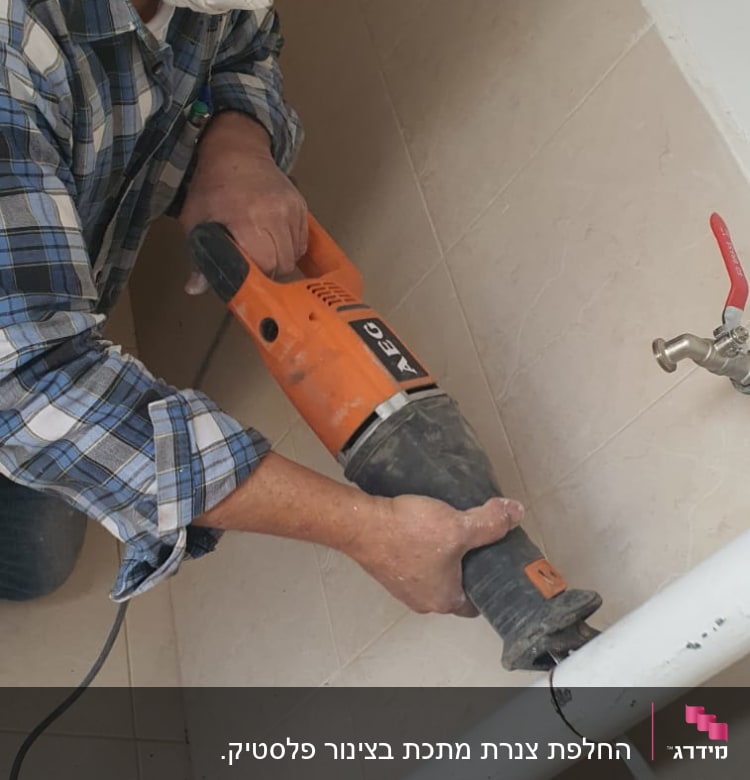 אדם חותך צינור עם מסור חשמלי כתום